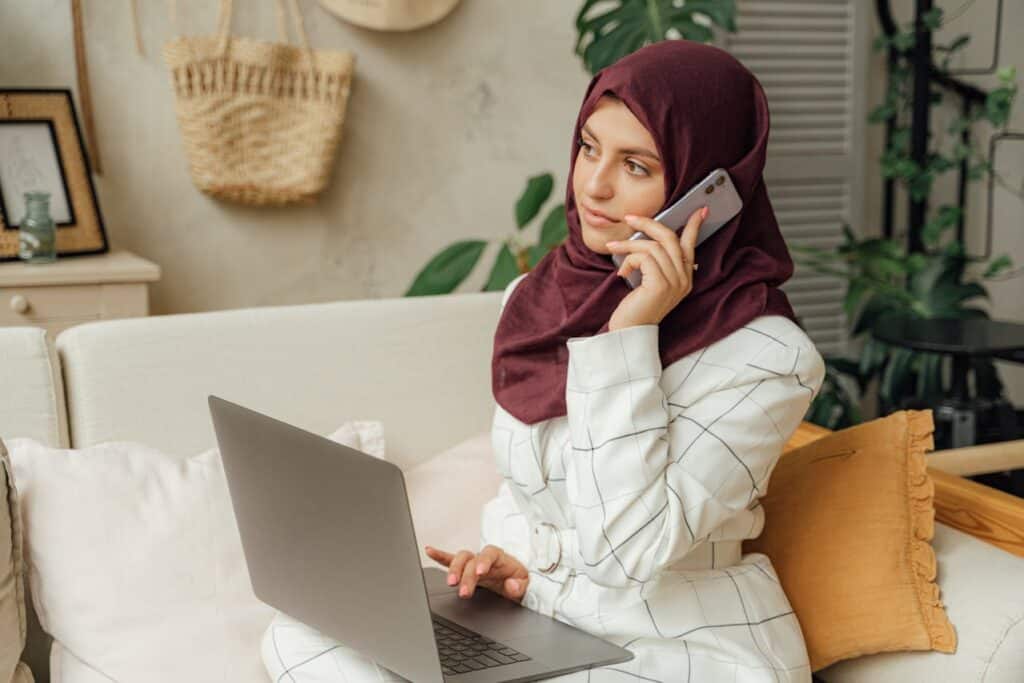 A Woman in a Hijab Using a Computer and Talking through the Phone