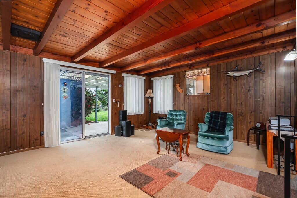 Rustic family room with wood-beamed ceilings, wood paneling, cozy arm chair and glass sliding doors that lead out the yard at 1751 39th Street