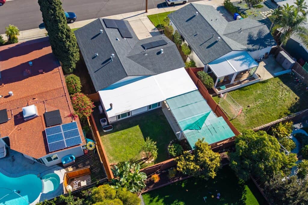 Aerial view of residential rooftops in North Park featuring modern solar panels, backyards with lush landscaping, and a swimming pool.
