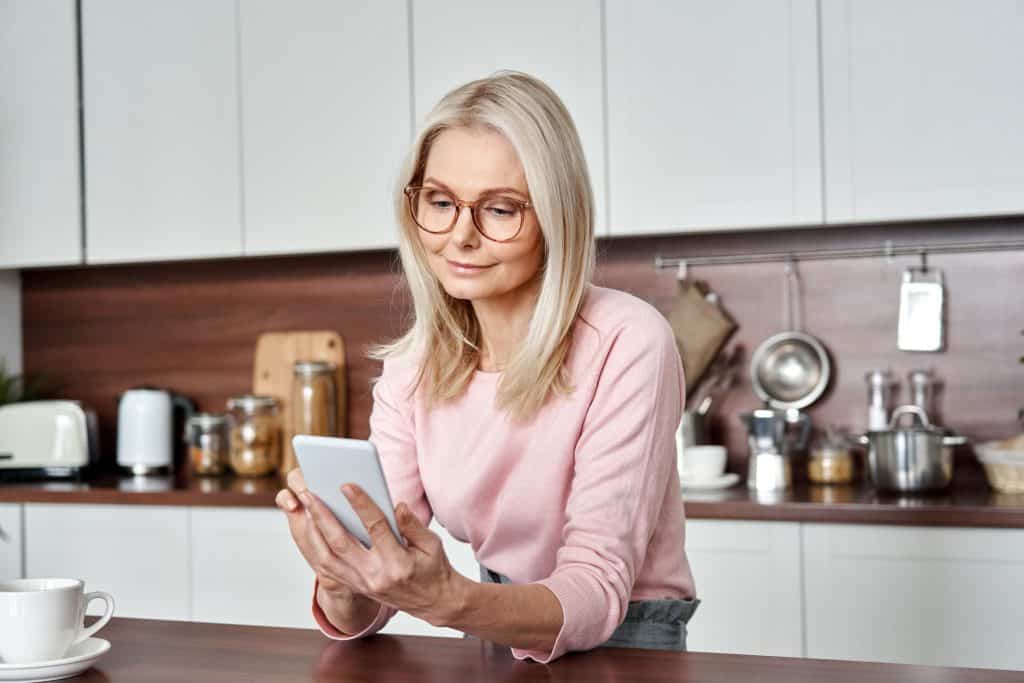Woman sitting in her kitchen looking at her online dating app.