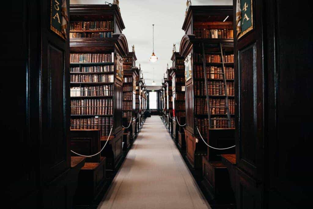 An aisle between massive wooden bookshelves in Marsh’s Library, stacked with ancient leather-bound books. Wooden ladders lean against the shelves for access to higher volumes.