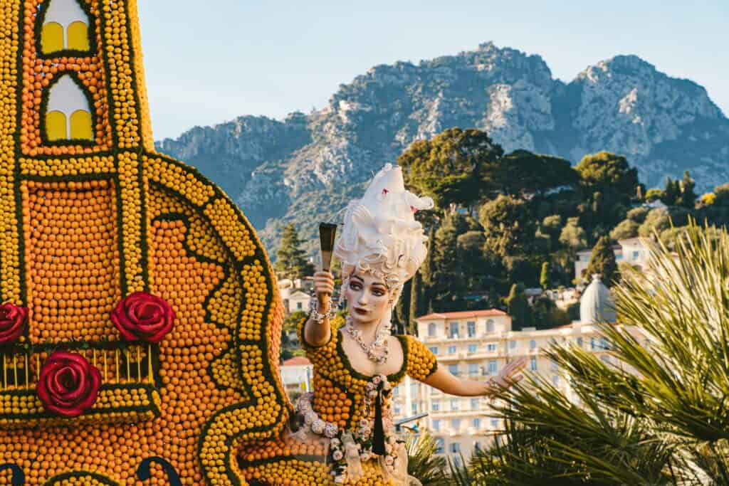Citrus-covered festival sculpture with the Alps and town rooftops behind it in Menton. The Fête du Citron is a major attraction in February.