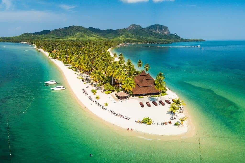 26 Beautiful Islands in Asia to Add to Your Bucket List 2024 7 a white sand beach is covered in palm trees and in the shape of a finger it is surrounded by emerald green ocean and has a beach resort on the edge. it is one of the best asian islands in Thailand and Koh Mook