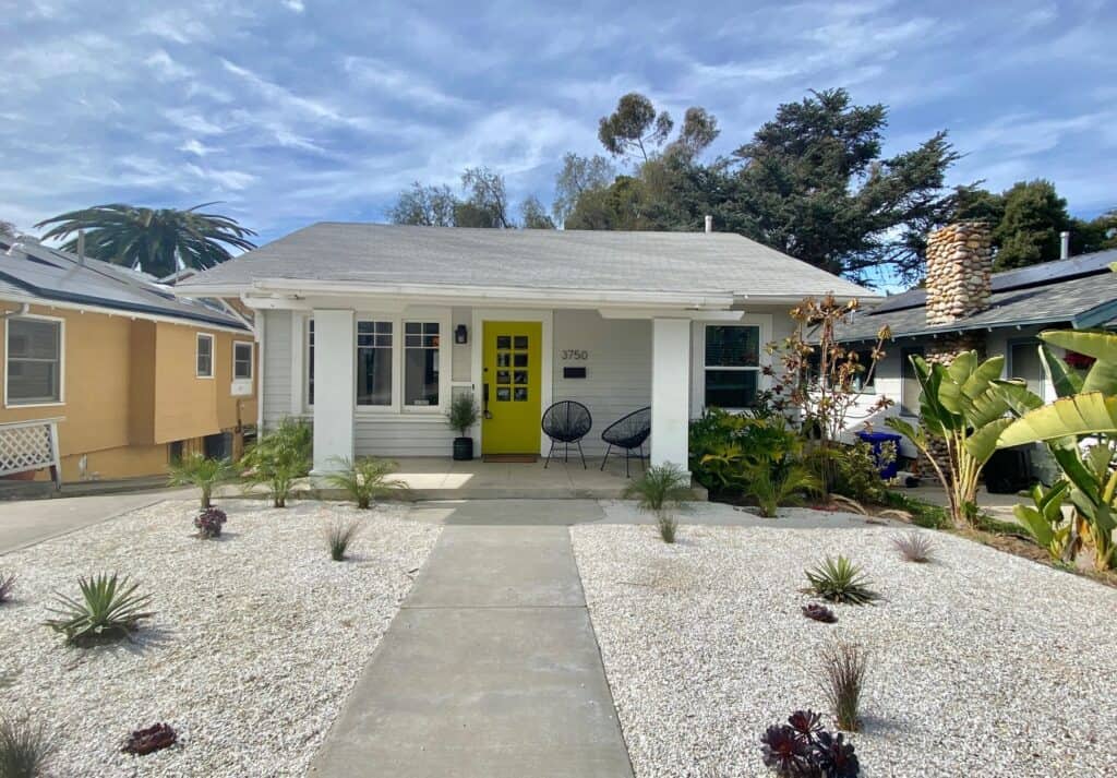 A charming, single-story home on Arizona Street in North Park, San Diego, featuring a bright yellow front door, white columns, and a xeriscaped front yard.