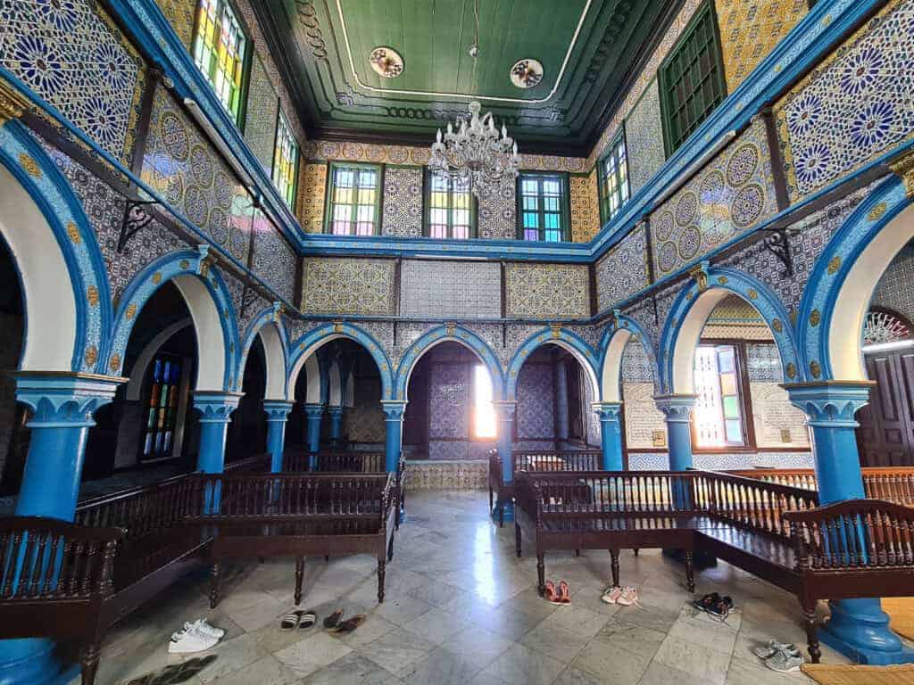 Colorful tiled interior of El Ghriba Synagogue in Djerba, Tunisia, with blue arches and stained glass windows