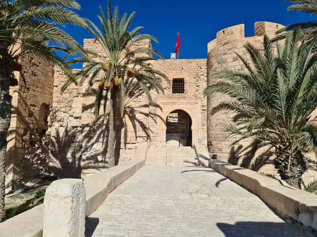 Entrance of the historic Borj El Kbir fortress in Djerba, Tunisia, surrounded by palm trees and blue sky