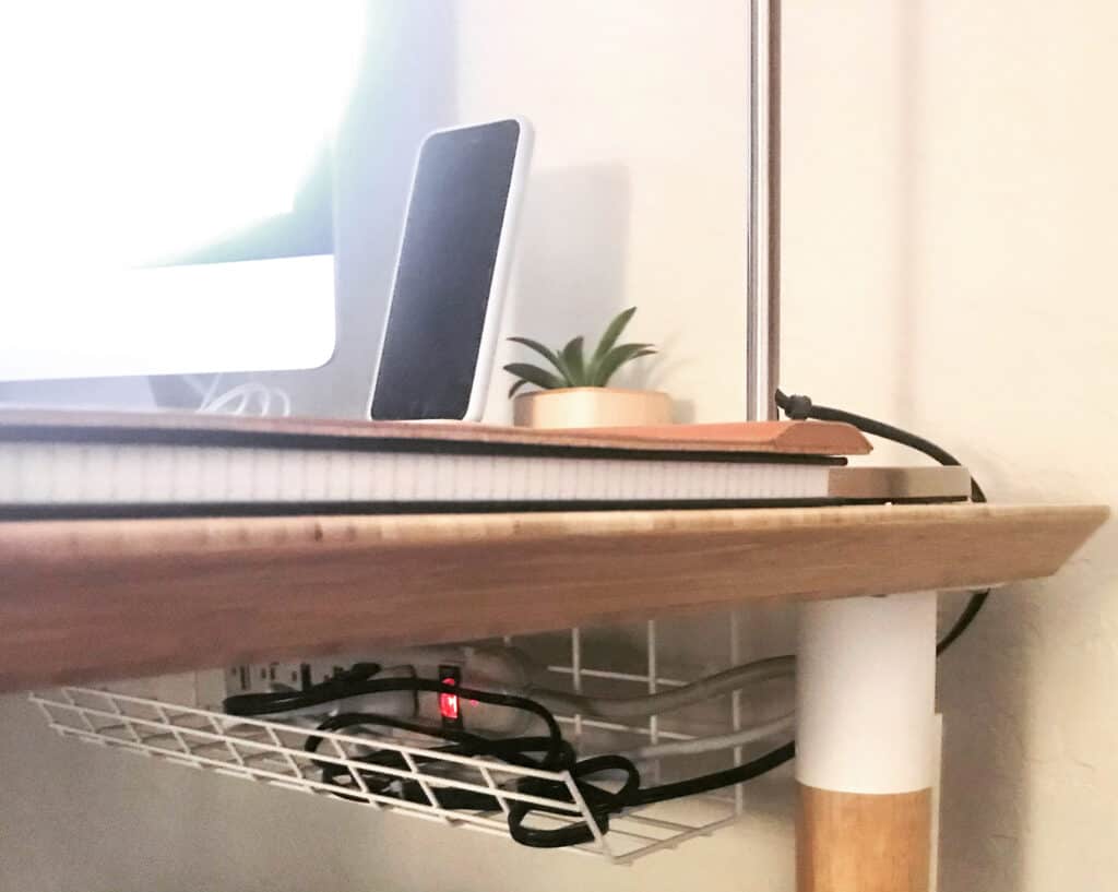 A home office desk with an under desk cable management box holding a surge protector