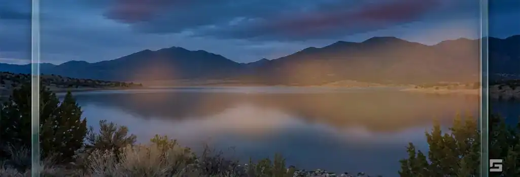 A serene New Mexico twilight lake viewed through a clear glass overlay with a warm amber glow, representing fish and game violation defense. Legal resources from Grano Law Offices, P.C.
