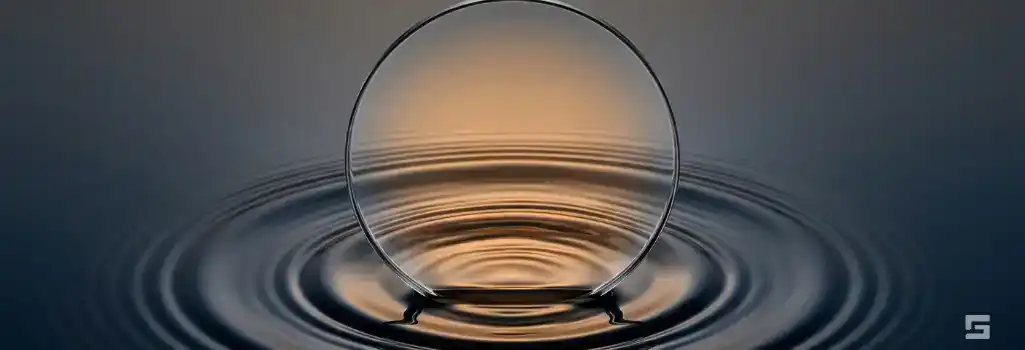 A clear glass lens focusing warm amber light over calm water ripples, representing the translation and clarity of personal injury legalese. Strategic civil litigation resources by Grano Law Offices, P.C.