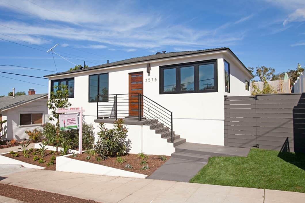 Modern, single-story home at 2576 Myrtle Ave featuring a crisp white stucco exterior with black-framed windows, a natural wood front door, and a sleek black metal handrail leading up the concrete entryway stairs.