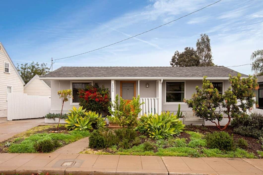 Single-story cottage at 2505 Boundary Street in North Park featuring a light grey exterior, a natural wood front door, and drought-tolerant landscaping with agaves, succulents, and a blooming red bougainvillea.