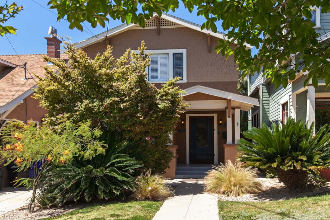 Two-story Craftsman home exterior featuring shake shingle siding, a covered front entry porch, a brick chimney, and lush tropical landscaping at 1630 Dale Street in South Park.