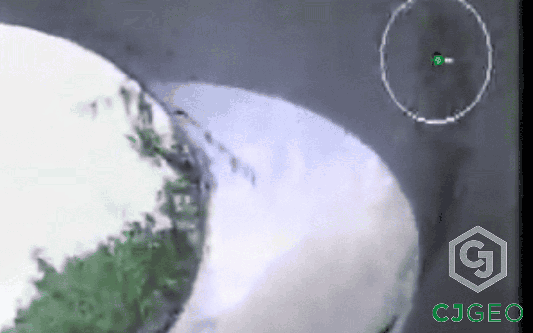 photo taken by a remote video crawler camera looking upstream out of a large concrete stormwater pipe, with the stream bank and sky in the background