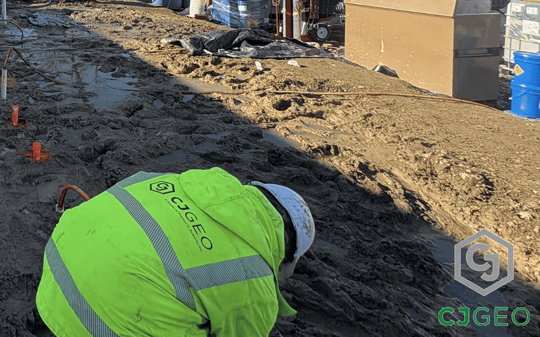 A CJGeo worker leaned over on a muddy jobsite with manchette tubes sticking out of the ground for permeation grouting.