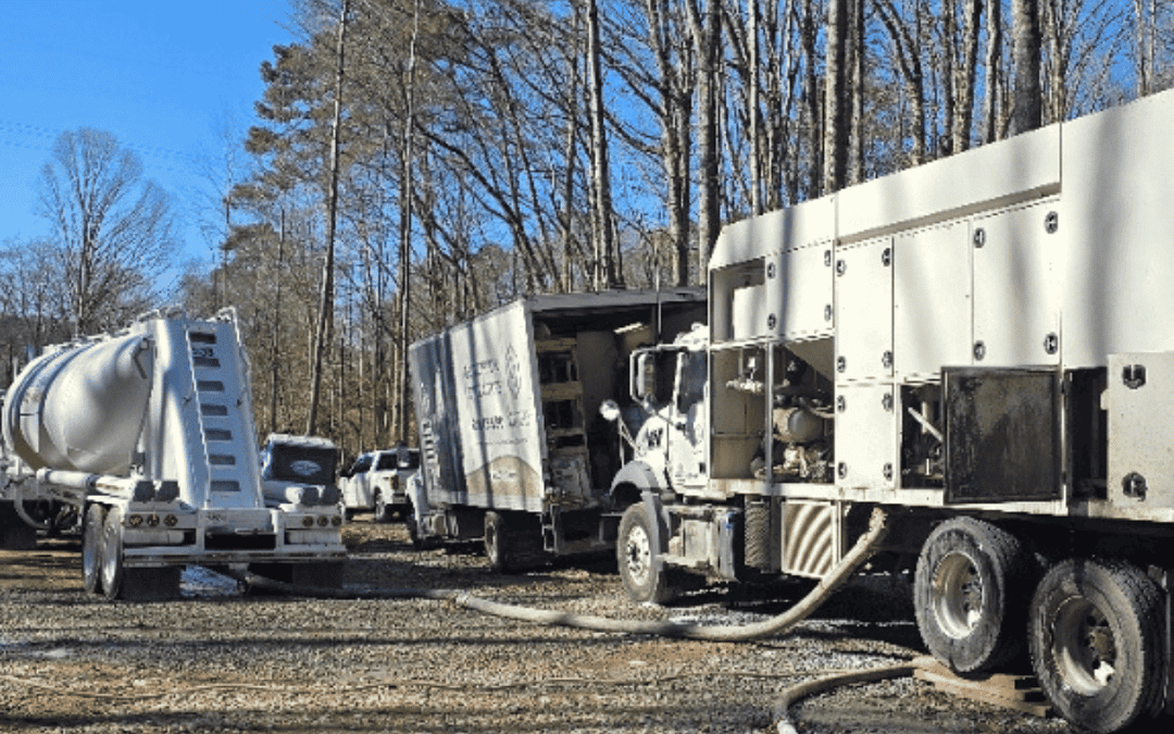 A large white CJGeo batch plant and support truck sit at a construction site in the woods.