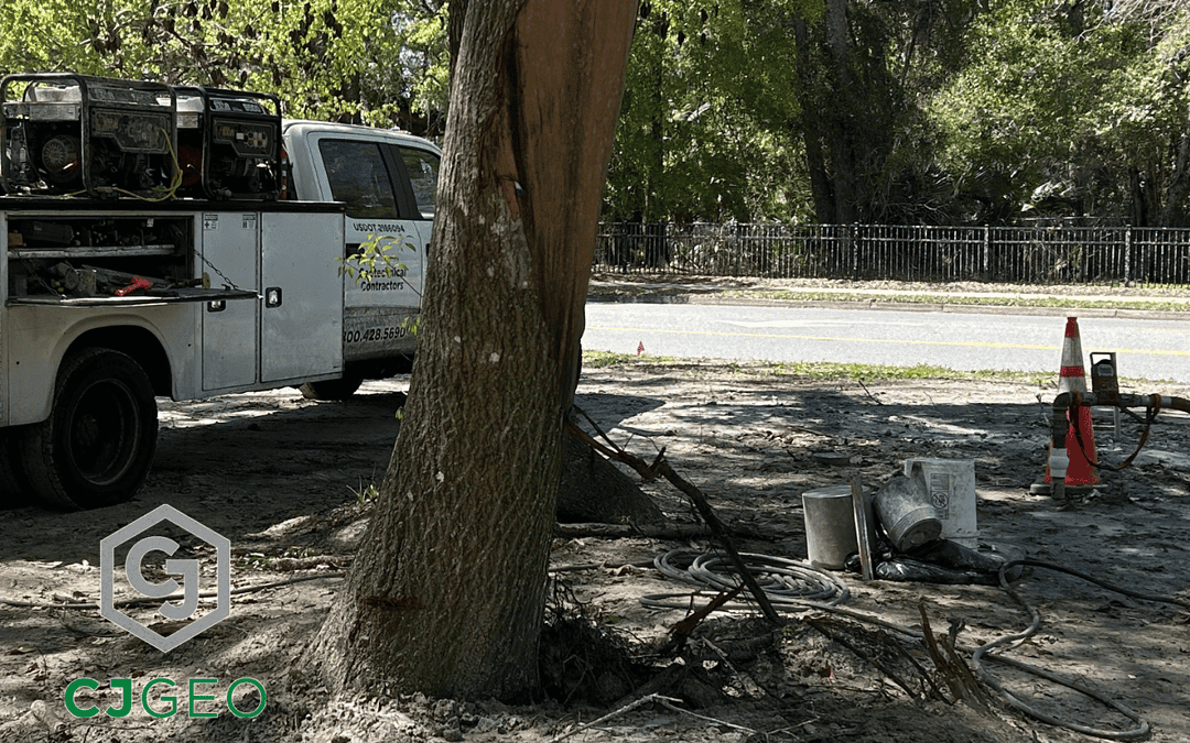 A CJGeo grouting truck and trailer in a forested setting with a grout hose connected to a pipe being filled with cellular grout.