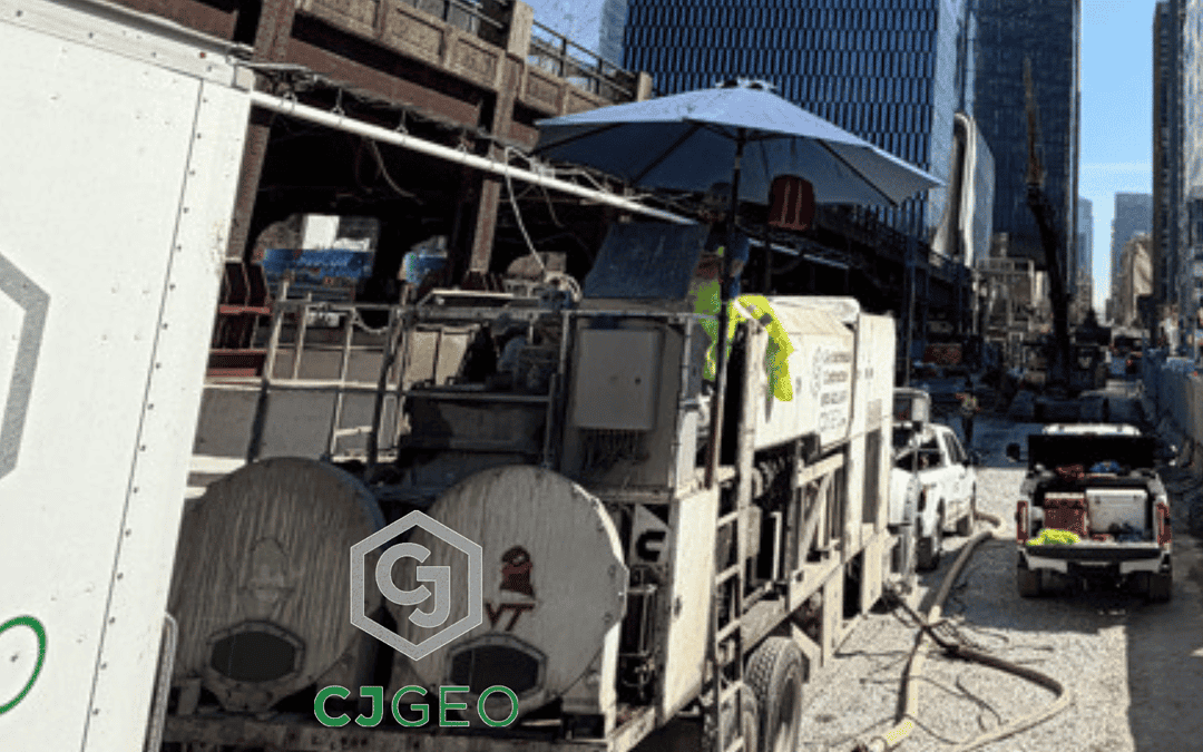 CJGeo cellular concrete batch plant onsite at a construction project with a bridge, fence, and Manhattan skyline in the background.