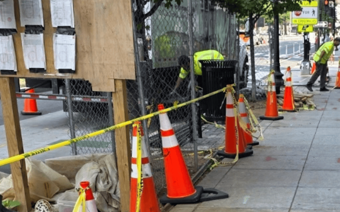 An urban construction site on a sidewalk with cones and a polyurethane grouting truck.