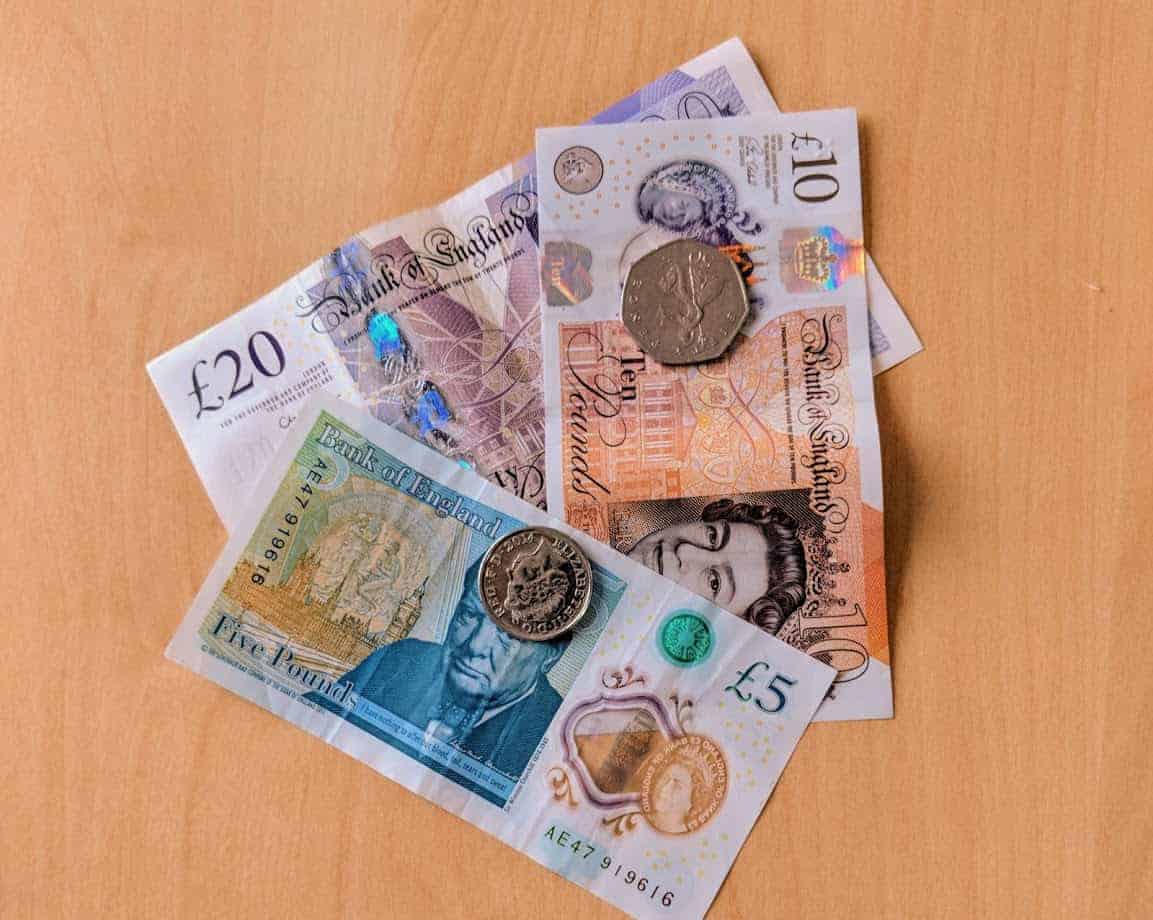 A mixture of British currency notes and coins on wooden table