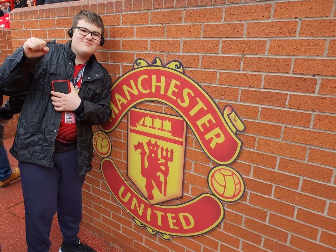 A young boy posing by the Manchester United sign on brickwork