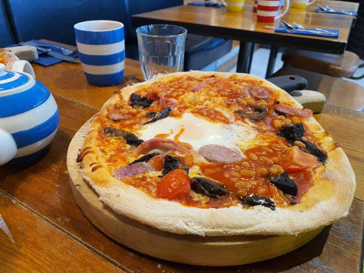 A pizza sitting on top of a wooden table with blue and white mugs