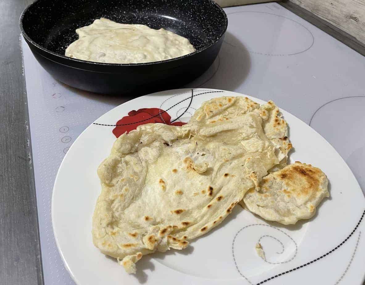 Frying pan with dough next to cooked flatbreads.