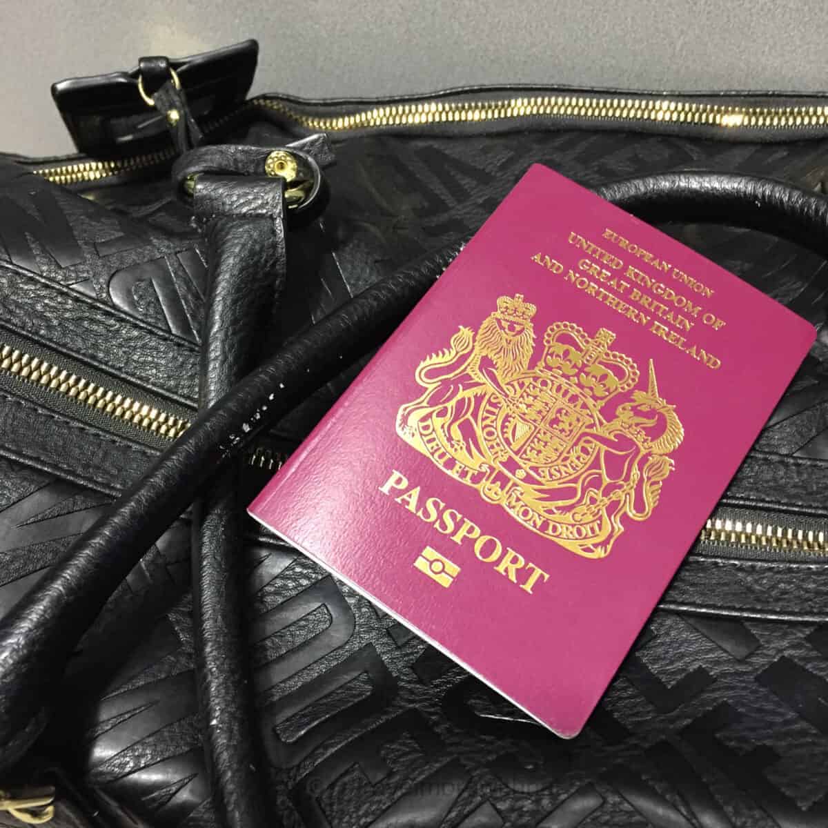 A burgundy UK passport sits on top of a black textured holdall bag. Keeping important items in the same bag pocket helps reduce stress when travelling with ADHD.