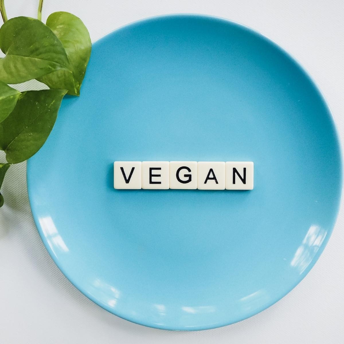 blue plate with scrabble letters spelling vegan on it and some leaves next to it