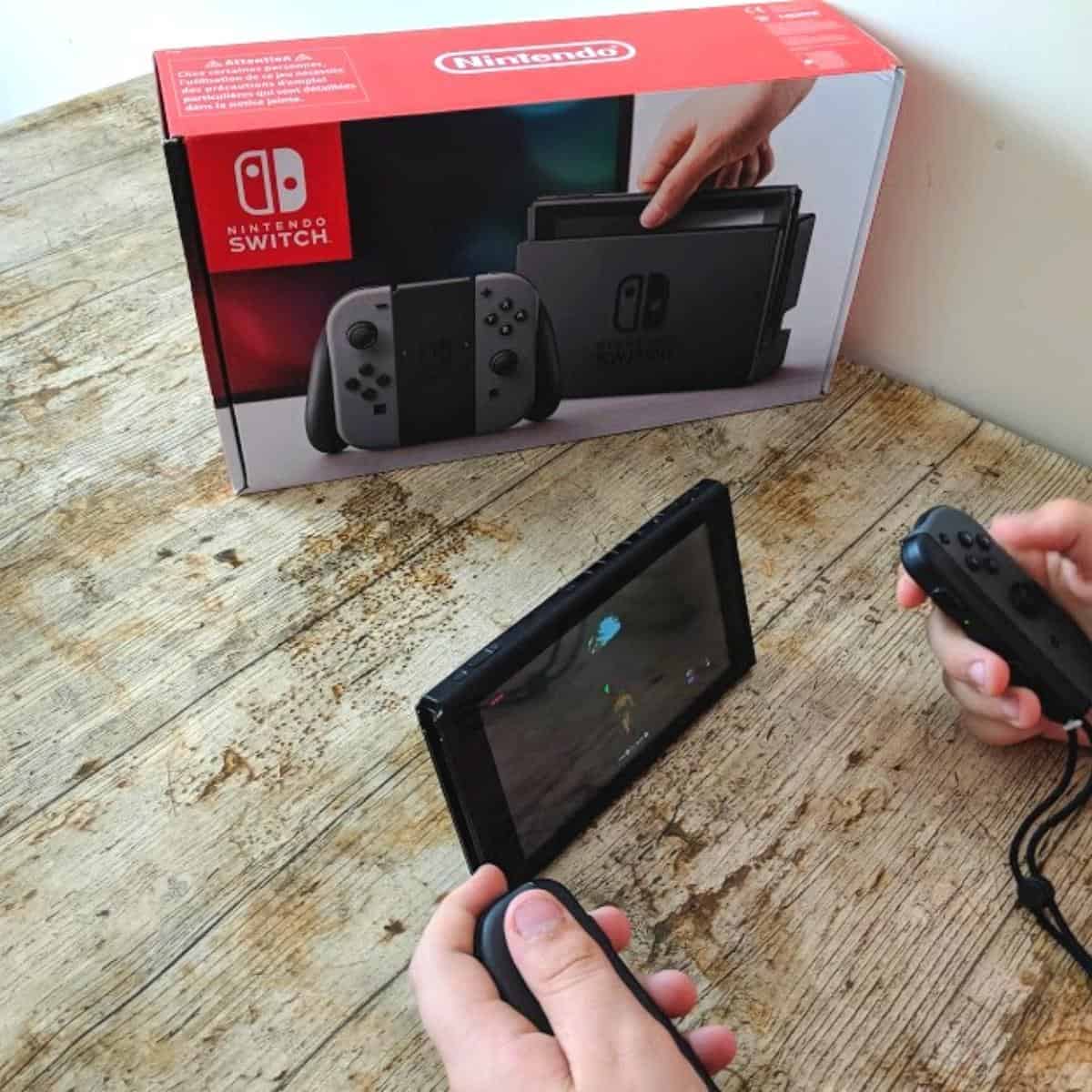 nintendo switch on a wooden table with a boys hands playing with it.