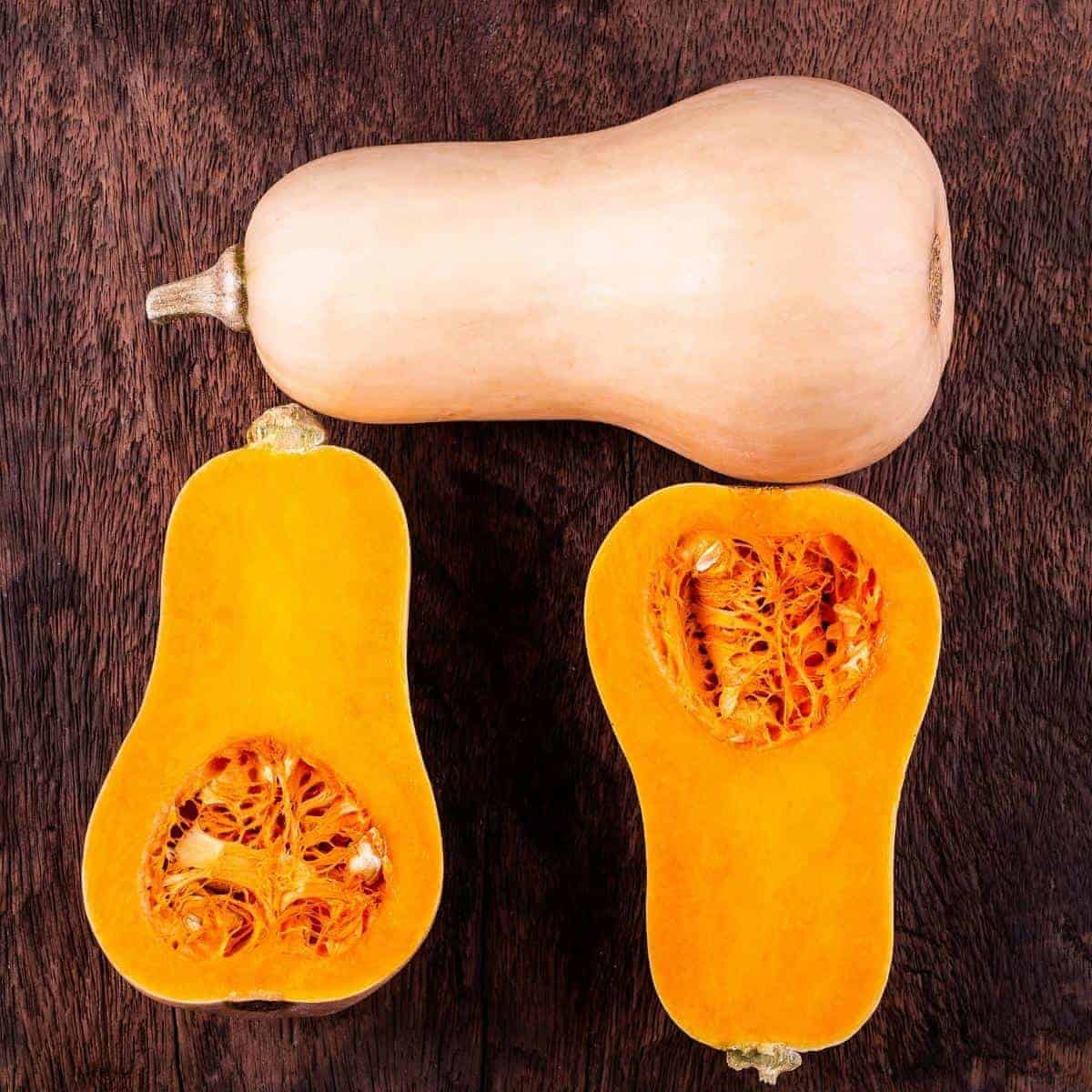butternut squash and another cut in half on a wooden table.