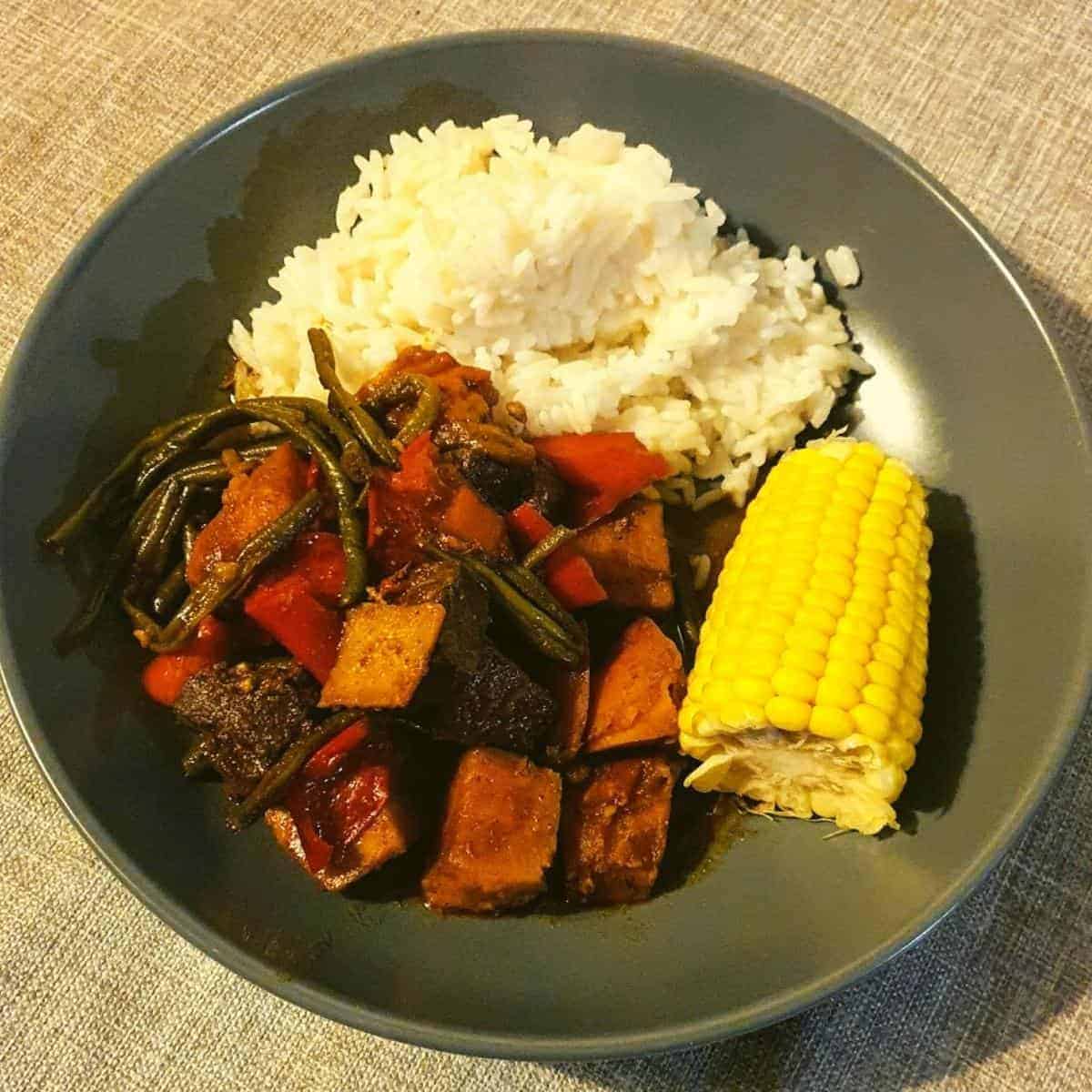 bowl of rice with caribbean pepperpot stew and a corn on the cob