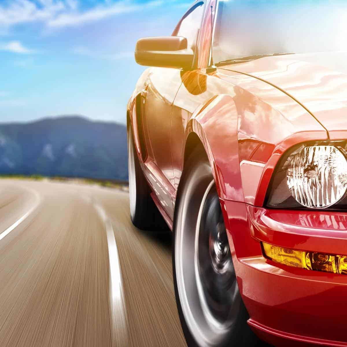 Closeup of red car with road and landscape in background