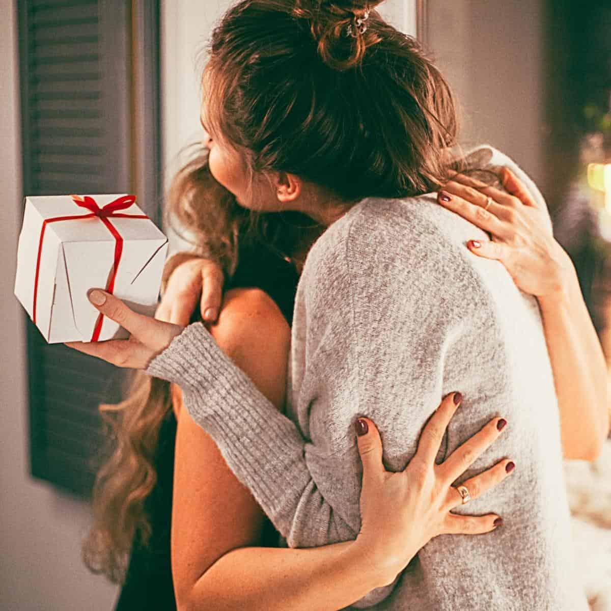 mothers day mum cuddling adult daughter holding a gift.