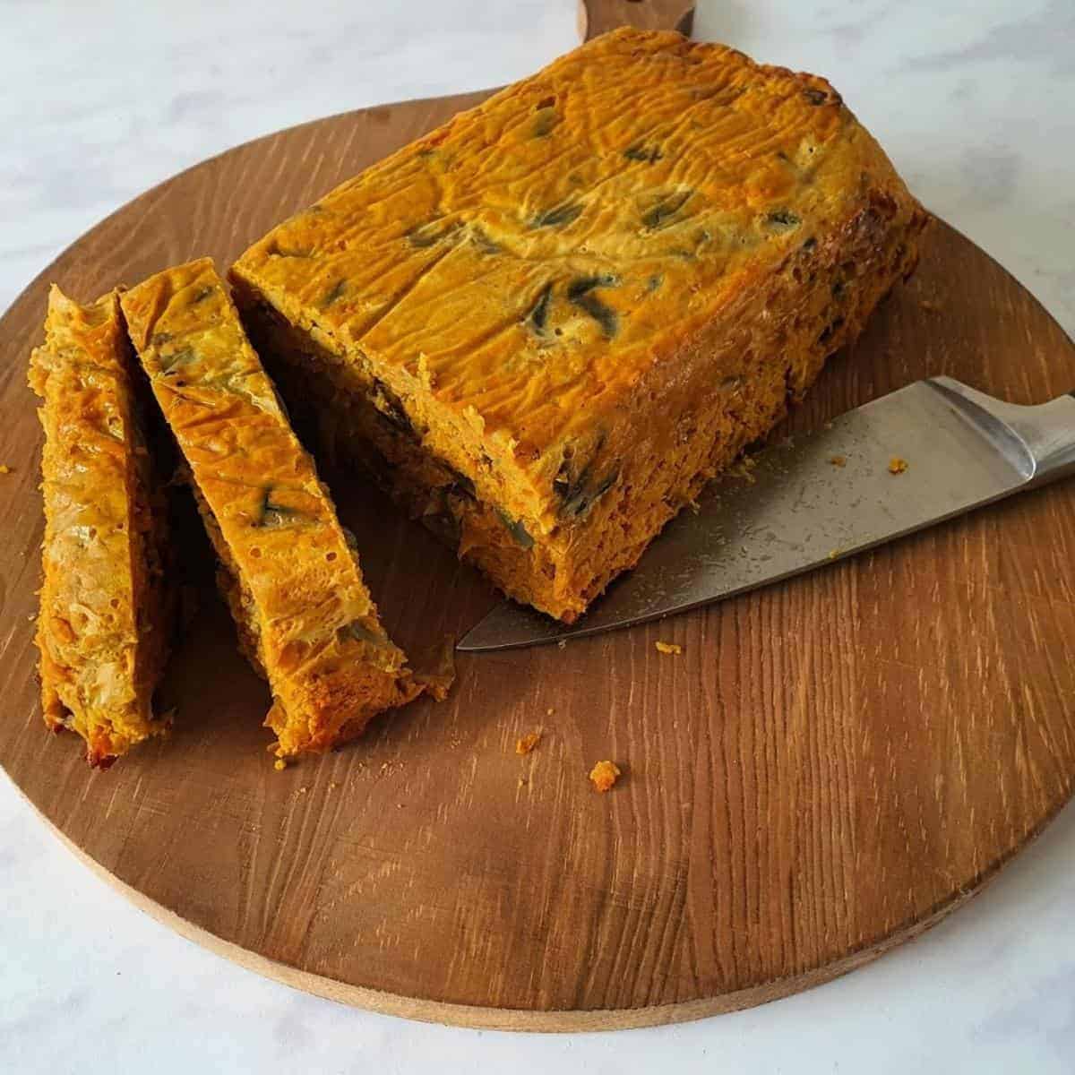 curry loaf on round wooden board with large knife