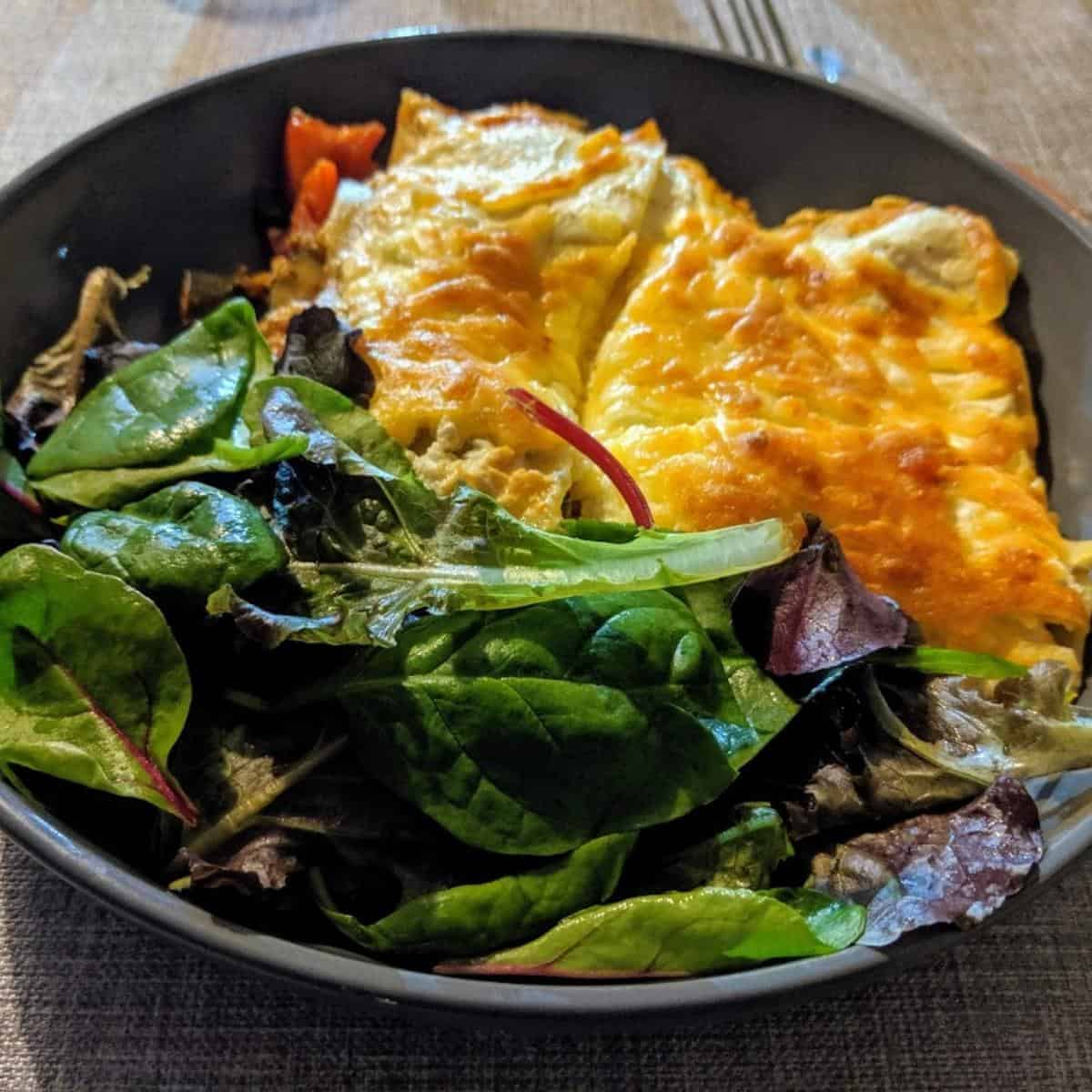 gray bowl with salad leaves and a vegetable lasagne