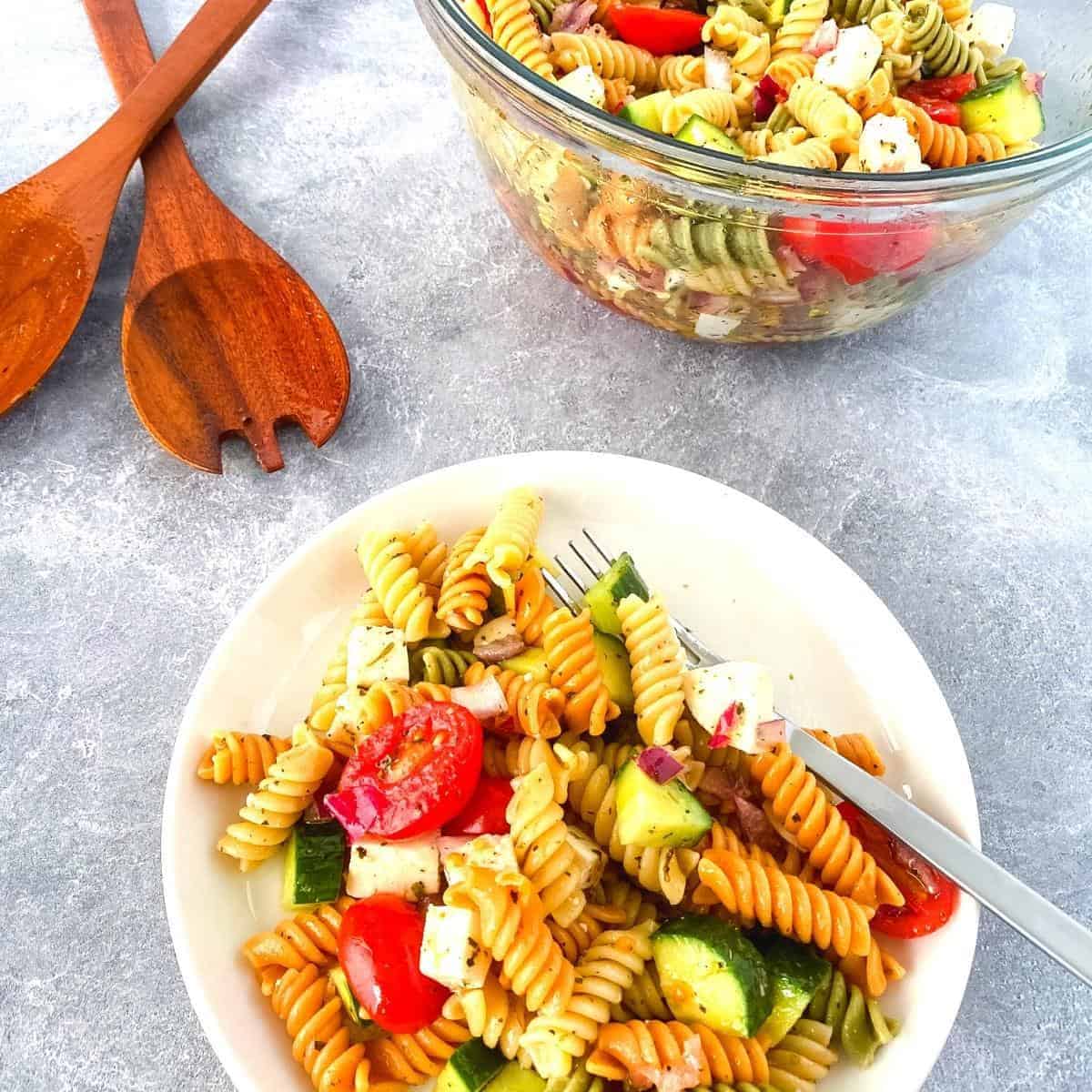 pasta salad served on a plate next to a bowl of pasta salad
