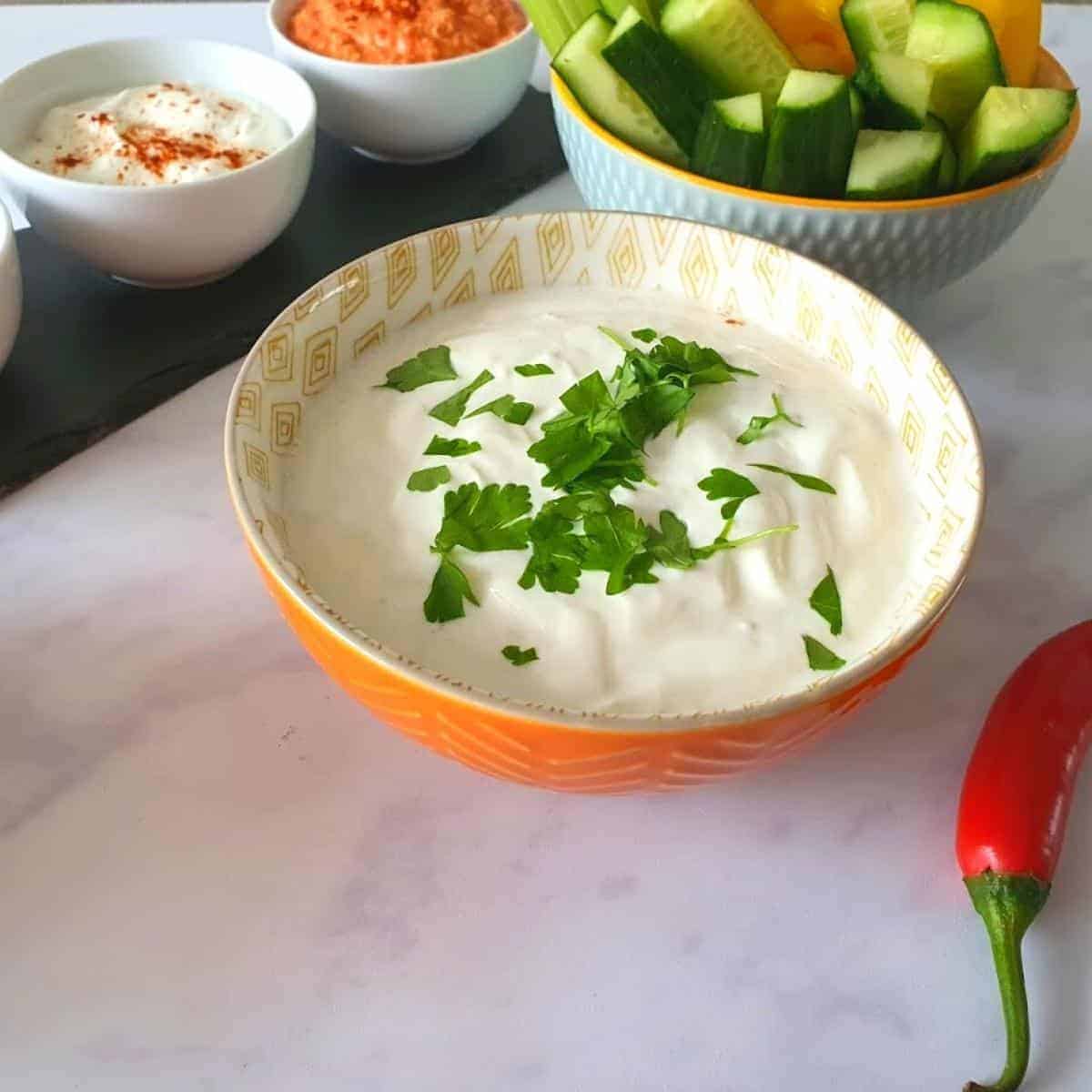 garlic dip in an orange bowl with other dips in background