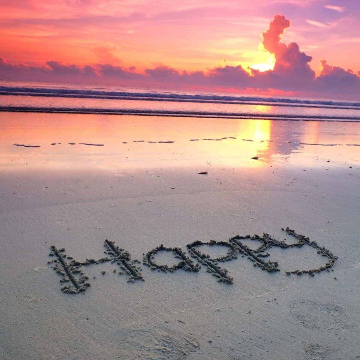 happy written in the sand at sunset