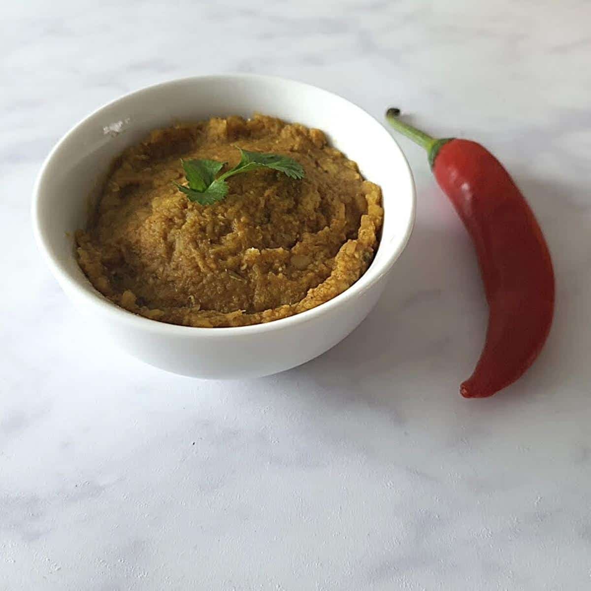white bowl of spicy lentil dip with a red chilli beside it for decoration