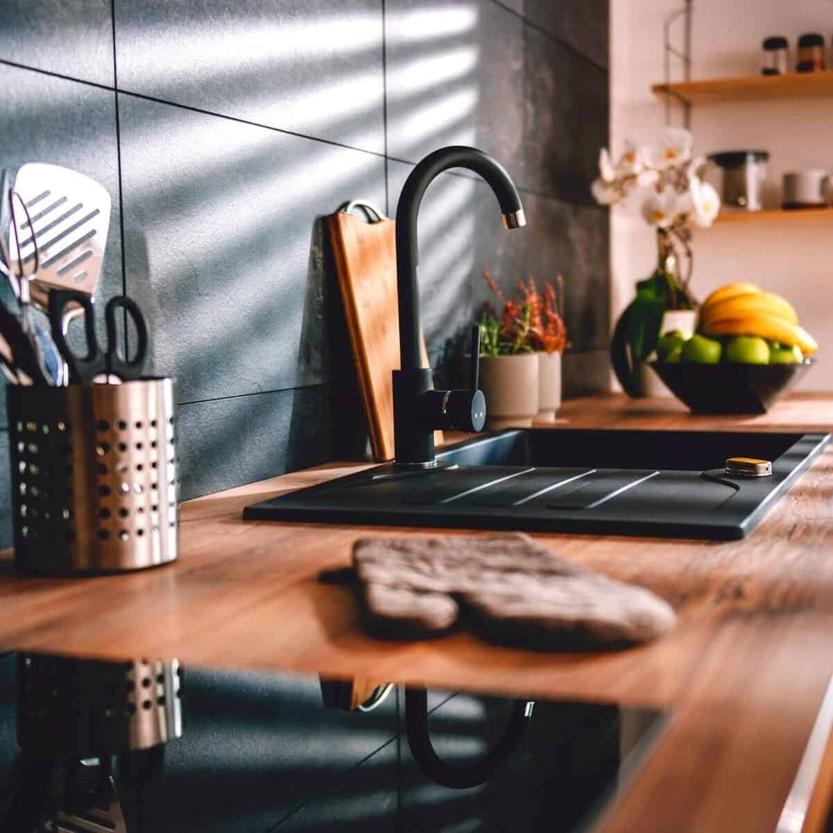 Tidy kitchen worktop with black sink and utensils in a pot.