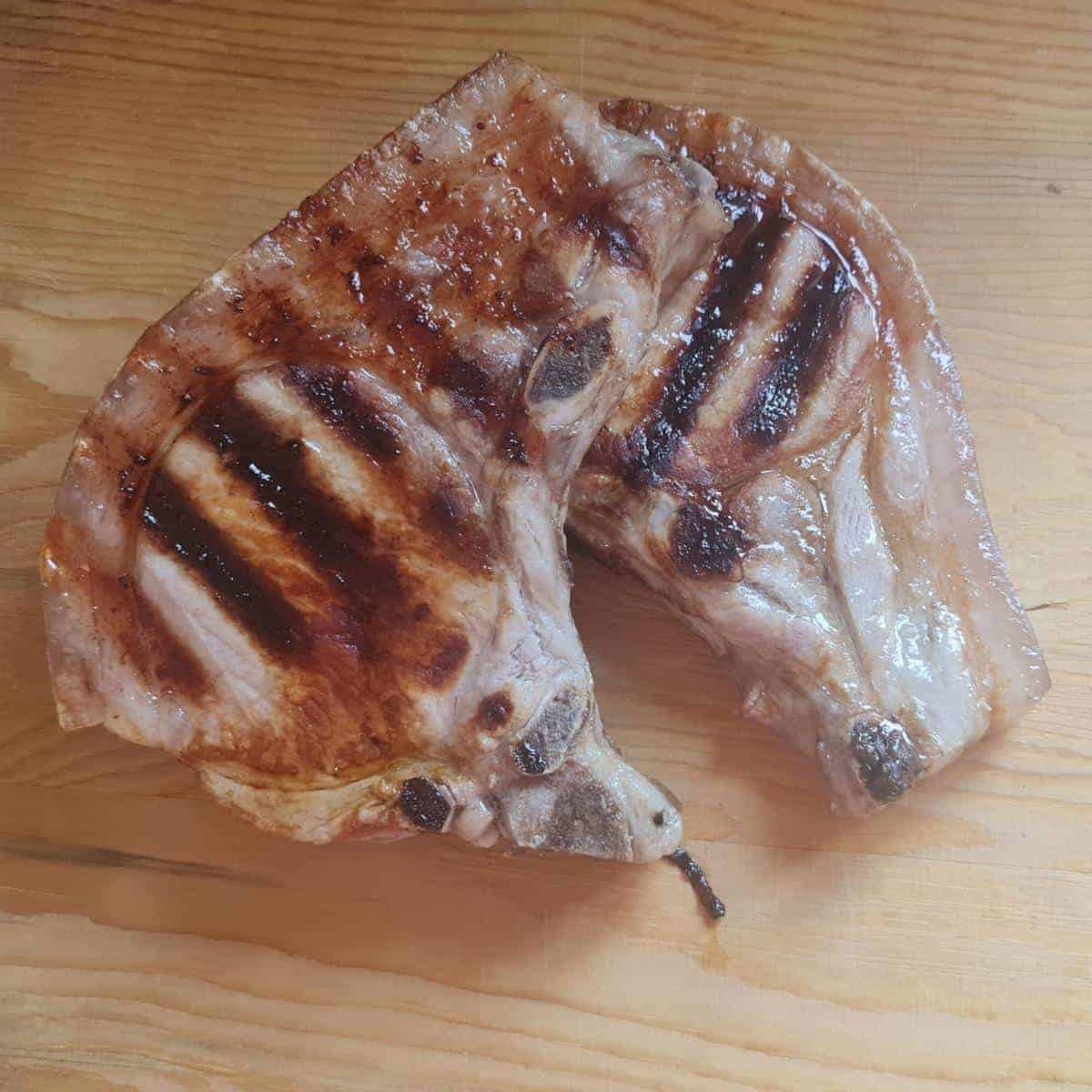 A close up photo of two pork chops cooked with grill lines on a wooden board