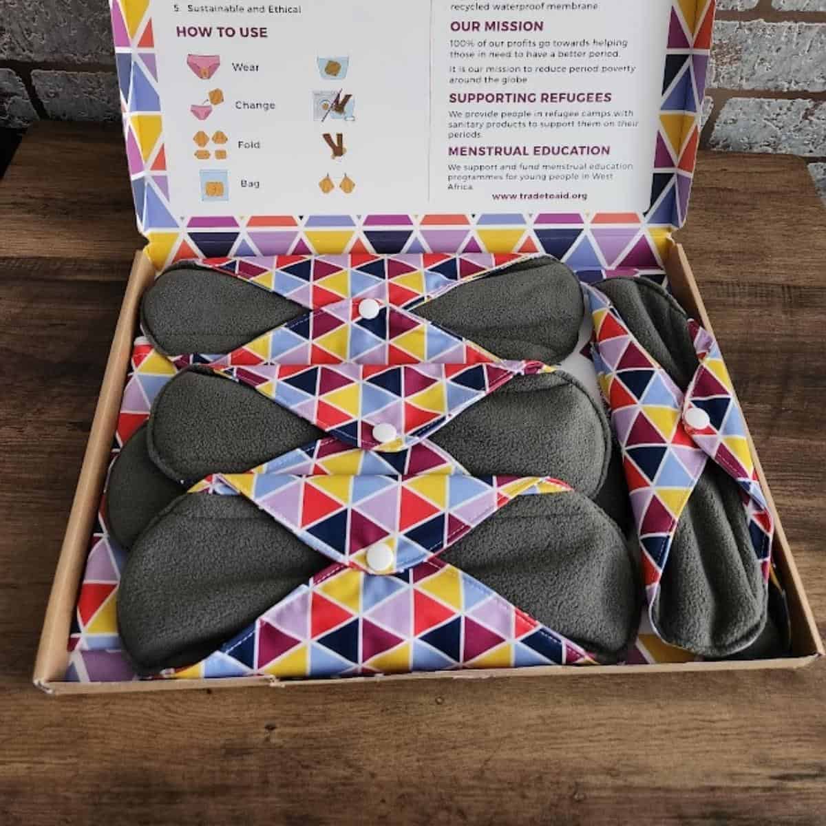 A box of reusable sanitary pads with colorful geometric patterns, featuring information on sustainability and usage.