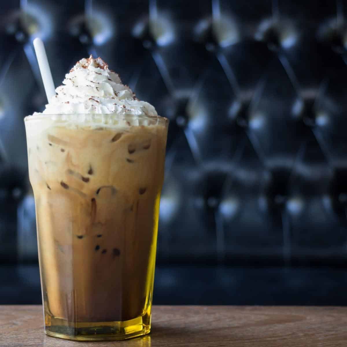 Whipped coffee topped wiht cream with a straw in a glass on a wooden table.