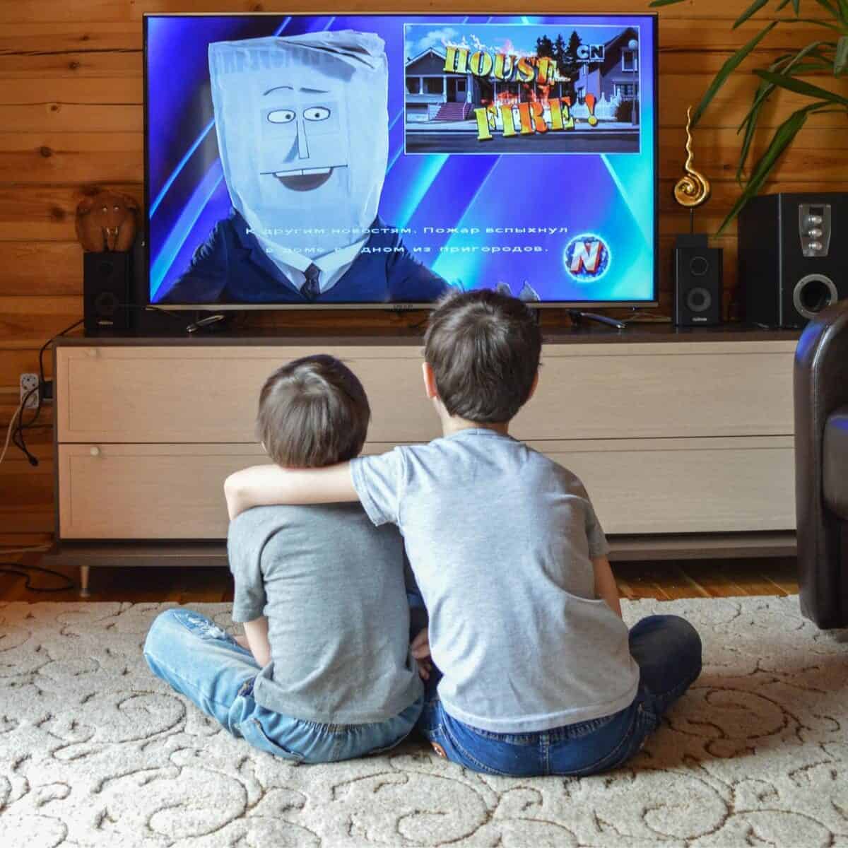two boys sitting on a rug watching tv