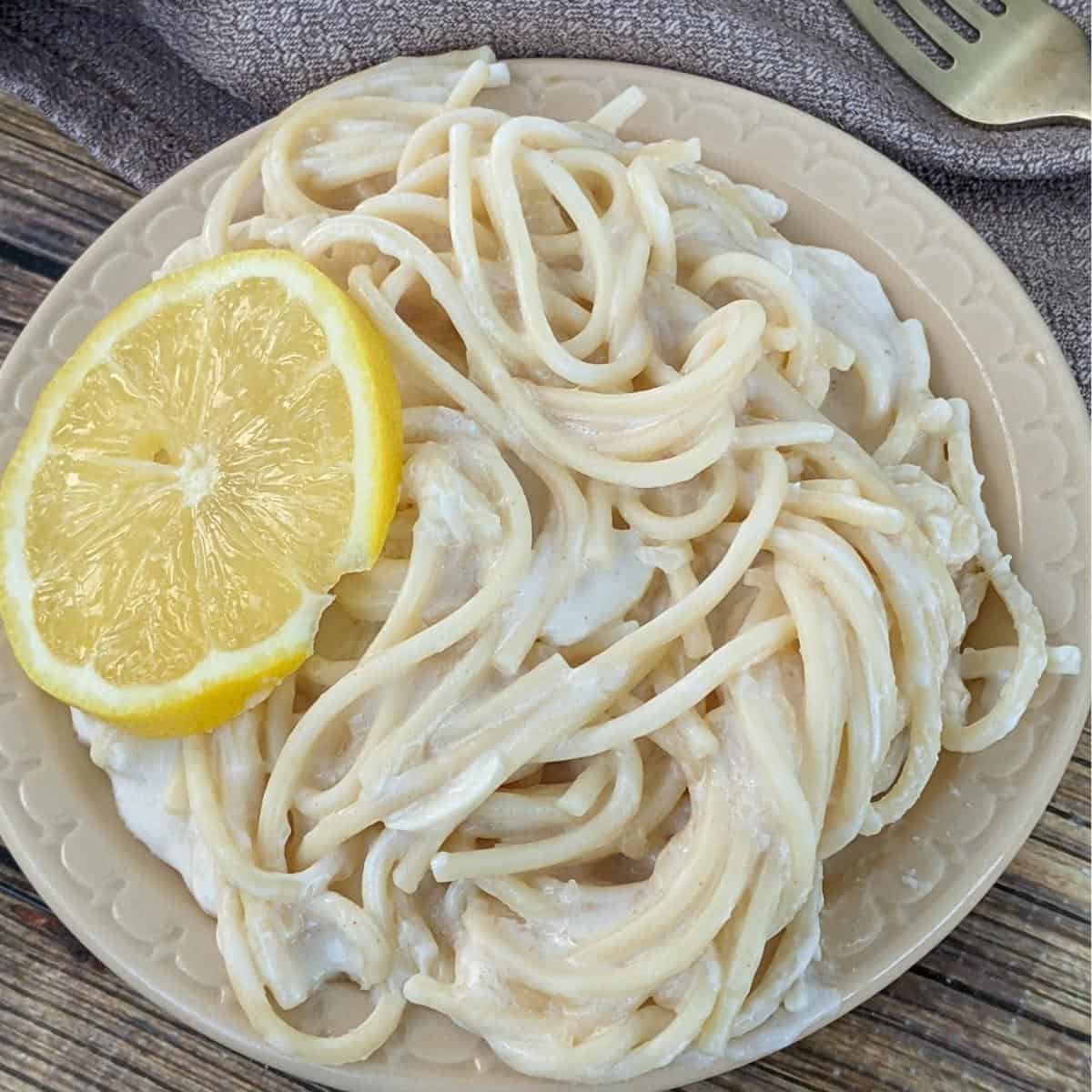Plate of lemon spaghetti topped with a slice of lemon.