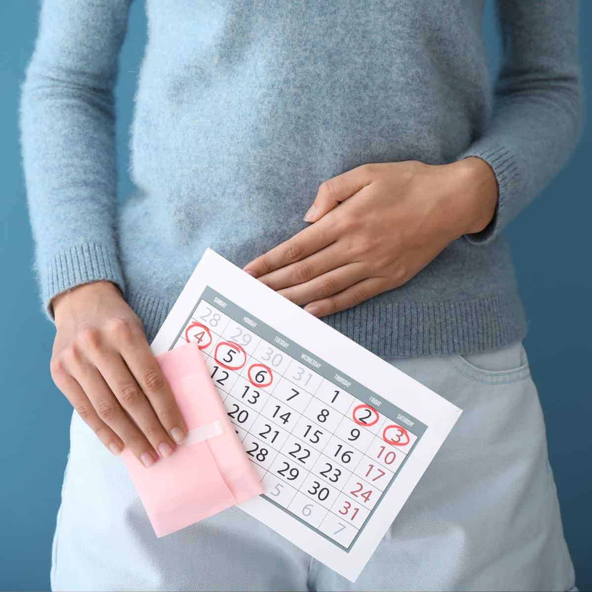 Woman holding her stomach and a calendar due to her period.