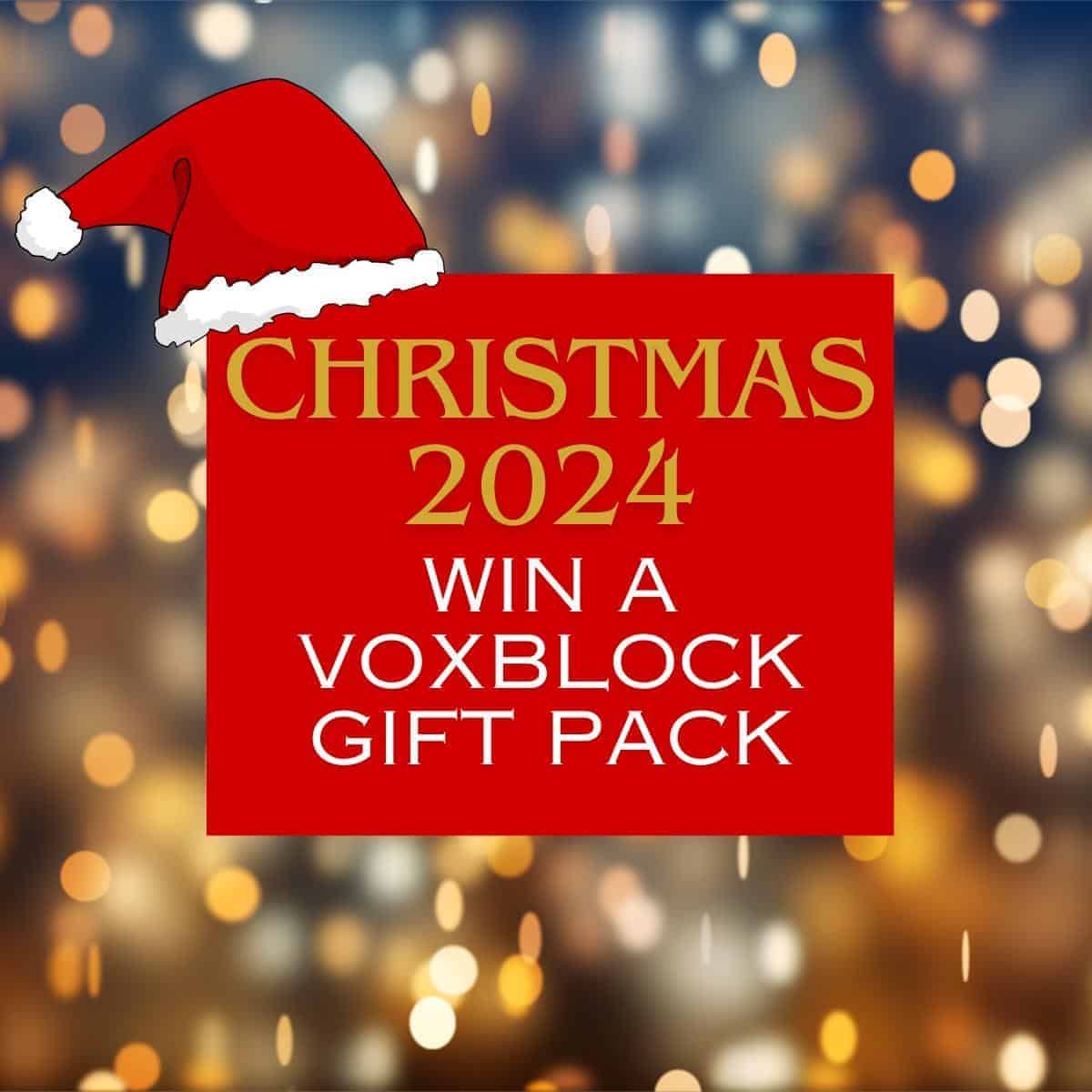 Red sign with a Santa hat reading "Win a £59.99 Voxblock Gift Pack for Christmas 2024" against a blurred festive light background.