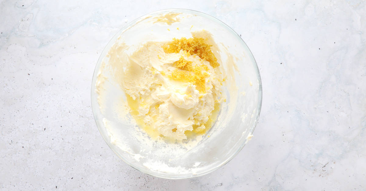 A glass mixing bowl containing butter, sugar, lemon zest, eggs and flour.