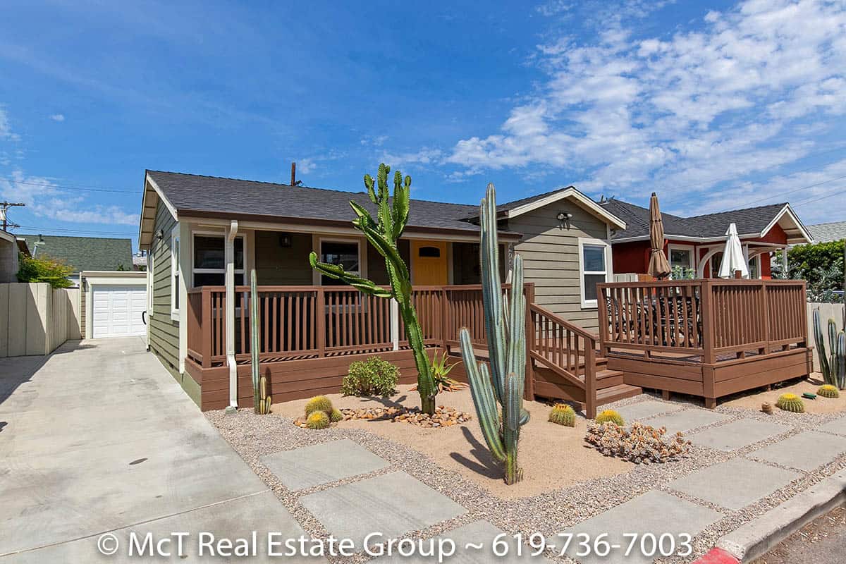 Front exterior of a University Heights bungalow home featuring a wooden deck, concrete driveway leading to a detached garage, and drought-tolerant desert landscaping.