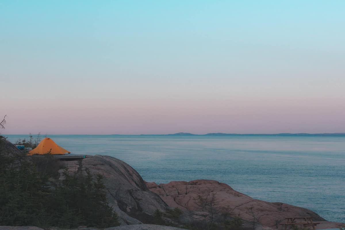 Ett oranget tält på klipporna vid havet.